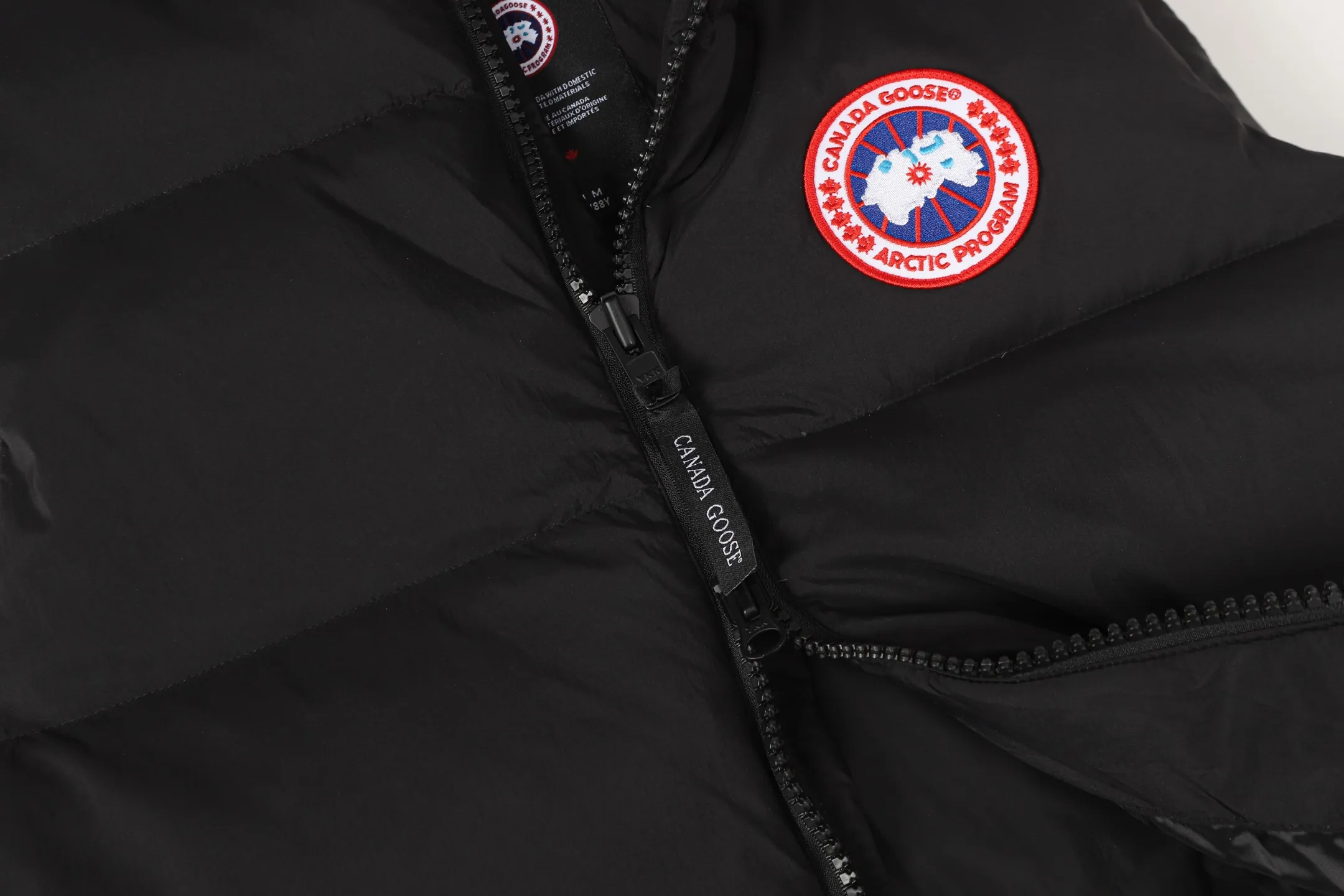 P560 Canada gooes Lawrence down vest (high version) The Lawrence down vest features a durable shell and quilted body, making it a must-have item for all seasons. The fabric has a durable soft touch. Longer hem at back for added protection. Reflective double-stripe grip tape at back. The Lawrence features an engineered down-filled collar to block strong winds, a two-way front zip and a longer rear hem.  Color: black with red label, black with black label, desert color, ocean blue Size: XS-2XL